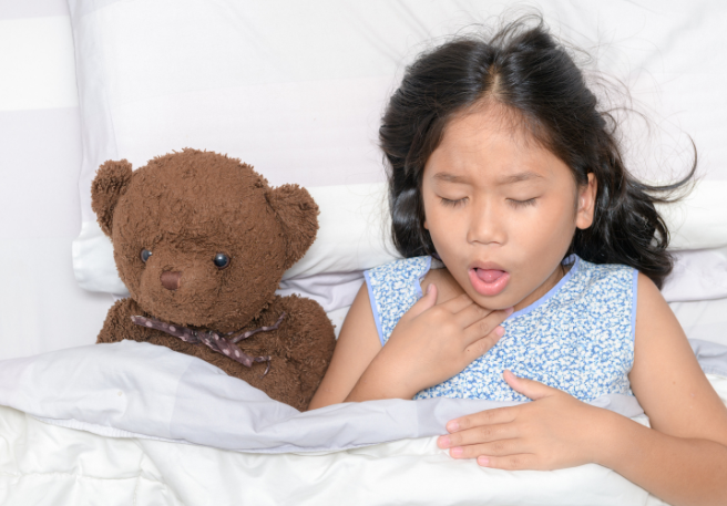 Mädchen liegt mit Teddybär im Bett und hustet